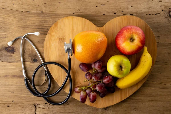 Close Heart Shape Apples Banana Orange Grapes Stethoscope Wooden Table — Stok fotoğraf