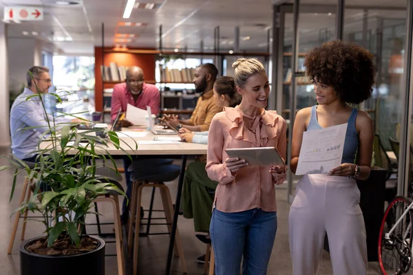 Mujeres Negocios Birraciales Sonrientes Discutiendo Juntas Contra Colegas Que Trabajan — Foto de Stock