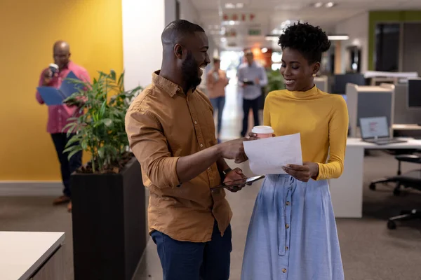 Happy african american businessman and businesswoman discussing over document at modern workplace. unaltered, business, teamwork and modern office concept.