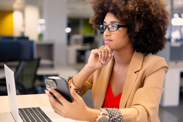 富有远见的年轻非洲裔美国女性顾问坐在工作场所 手持智能手机和笔记本电脑 现代办公和技术概念 — 图库照片
