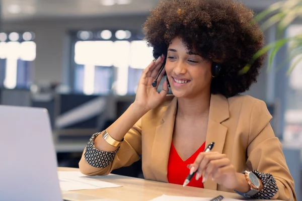 微笑着年轻的非洲裔美国女顾问一边在现代工作场所工作一边在耳机上说话 现代办公和技术概念 — 图库照片
