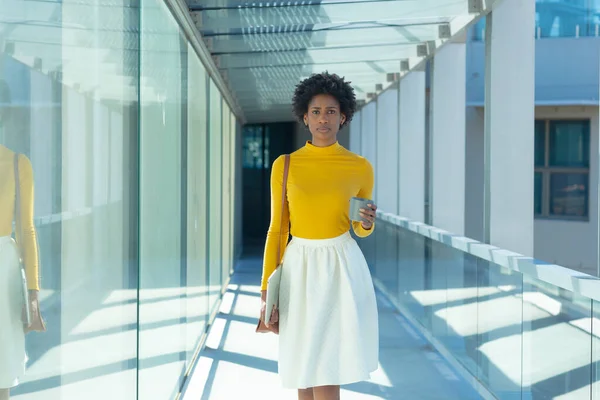 Portrait Confident African American Businesswoman Walking Mug Tablet Corridor Unaltered — Stockfoto