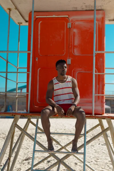 African American Young Man Looking Away While Sitting Lifeguard Hut — ストック写真