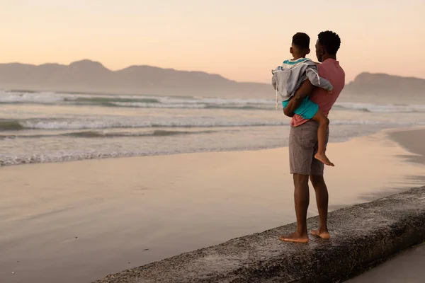 African American Young Man Carrying Son While Standing Rock Beach — стокове фото