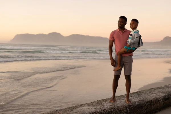 Sonriente Joven Afroamericano Llevando Hijo Mientras Está Pie Playa Contra — Foto de Stock