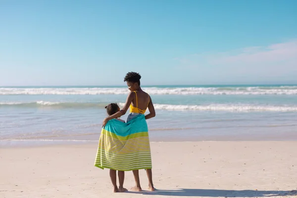 アフリカ系アメリカ人の若い母親と娘の後部ビューにタオルが空に対してビーチに立っている コピースペース 変更なし 子供時代 一緒に 楽しみ — ストック写真