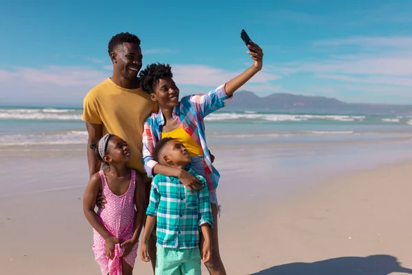 Happy african american young woman taking selfie with man, son, daughter over smartphone at beach. nature, summer, technology, unaltered, childhood, family, togetherness, enjoyment, holiday.
