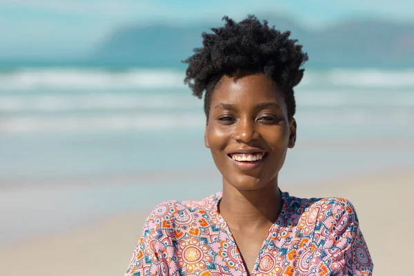 Close-up portrait of happy african american young woman with short curly hair against sea in summer. nature, unaltered, beach, lifestyle, enjoyment and holiday concept.