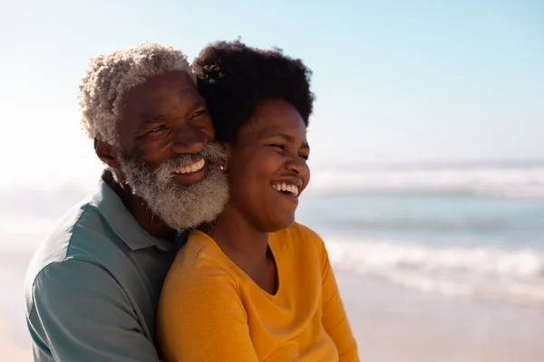 Romantic african american couple embracing and looking away while standing against sea and sky. happy, copy space, unaltered, love, togetherness, retirement, enjoyment and holiday concept.