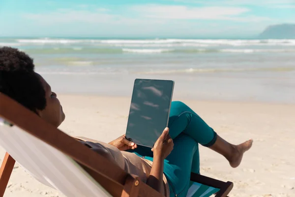 海と空に対してデッキチェアでリラックスデジタルタブレットを使用してアフリカ系アメリカ人の成熟した女性 無線技術 変わらない ライフスタイル 楽しみと休日の概念 — ストック写真