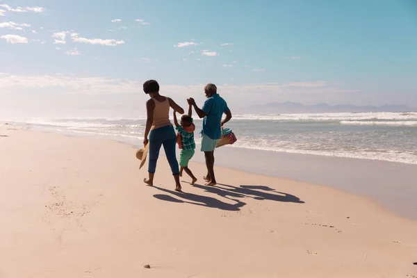 アフリカ系アメリカ人の祖父母が少年の手を取り合い 青い空に向かって砂浜を歩く コピースペース 変更なし 子供時代 楽しみと休日 — ストック写真