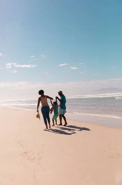 アフリカ系アメリカ人の祖父母は孫の手を取り合い 青い空を背景に砂浜を歩く コピースペース 変更されていない 一緒に 子供時代 楽しみ — ストック写真