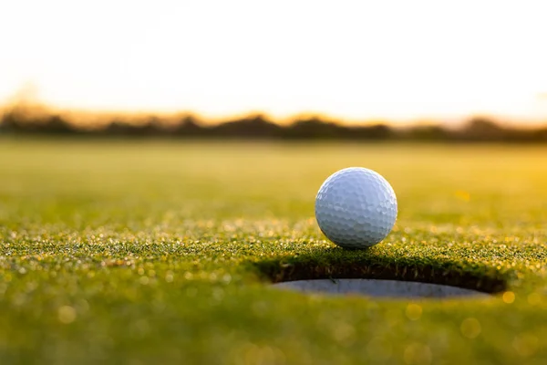 日没の間に澄んだ空に対して草原の土地に穴によって白いゴルフボールのクローズアップ スペースをコピー 変更なし ゴルフコース スポーツと自然の概念 — ストック写真