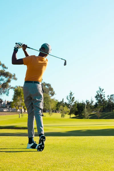 アフリカ系アメリカ人の若い男がゴルフコースで澄んだ空に対してゴルフクラブで打つの背面図 コピースペース ゴルフ 変更なし スポーツや週末の活動のコンセプト — ストック写真