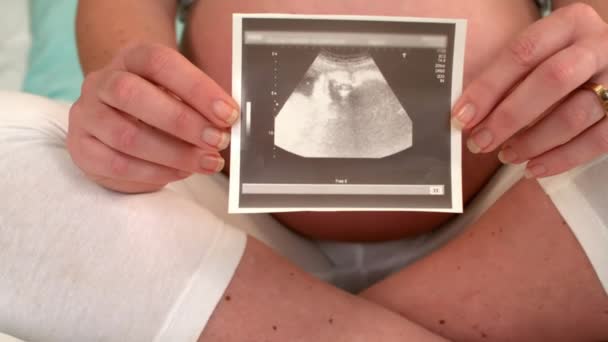 妊娠中の女性がベッドの上に座ってエコーを示す — ストック動画