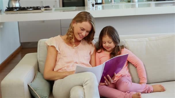 母亲带着女儿在家里的沙发上看书 — 图库视频影像