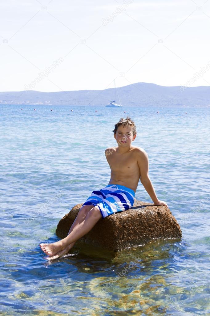 Cute Eleven Years Old Boy Sitting On A Rock In The Sea Stock Photo By 
