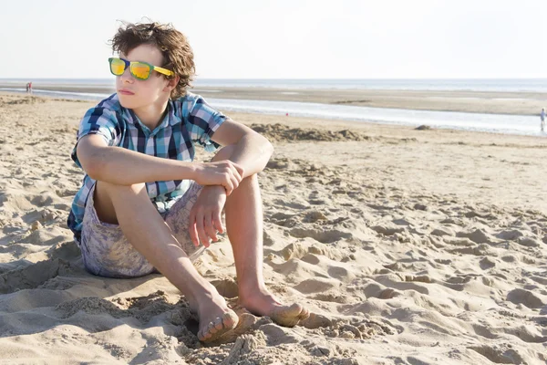 Tonårspojke som sitter på stranden — Stockfoto