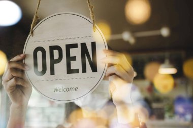 Korunan yüz maskesi takan Asyalı genç bir kadın modern kafe kahve dükkanındaki cam kapıyı açıyor, otel servisi, kafe restoranı, perakende mağazası, küçük işletme sahibi konsepti.
