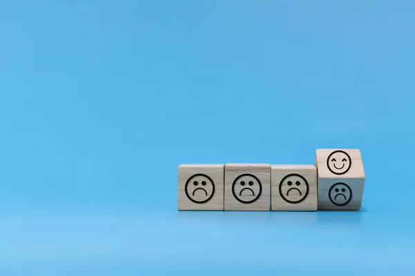 Happy and Unhappy emotion. happy smile face with sad face on wooden cube on blue background, positive think, social issues, customer satisfaction ,positive attitude, optimism and pessimism concept