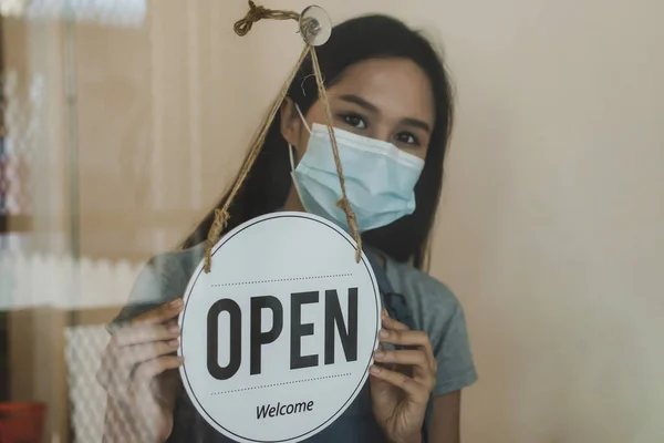 waitress staff wearing protection face mask turning Open sign board reopen after coronavirus quarantine is over in cafe coffee shop ready to service, reopen, cafe restaurant, food and drink concept