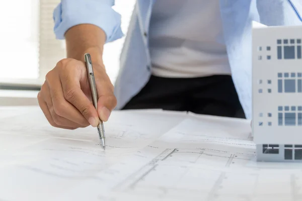 professional architect, engineer or interior hand reviewing blueprint with building model on workplace desk in office center at construction site, contractor, construction, engineering concept