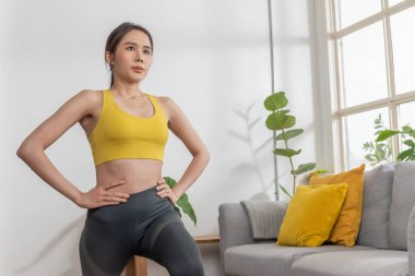 Spor kıyafetleri giyen genç, atletik Asyalı kadın evde oturma odasında spor yapıyor. Sağlıklı, vücut geliştirici, yaşam tarzı, spor, ev egzersizi konsepti.