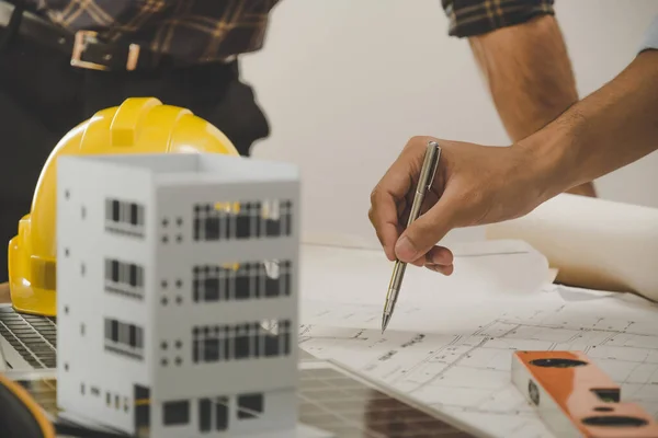 professional architect, engineer or interior hand reviewing blueprint with building model on workplace desk in office center at construction site, contractor, construction, engineering concept