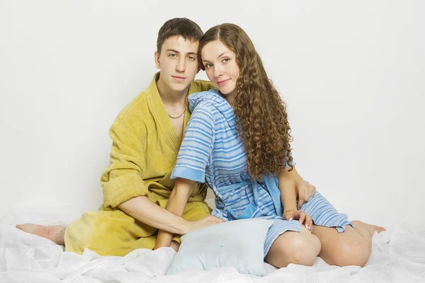 Junges verliebtes Paar auf einem Bett im Schlafanzug auf weißem Hintergrund Stockbild
