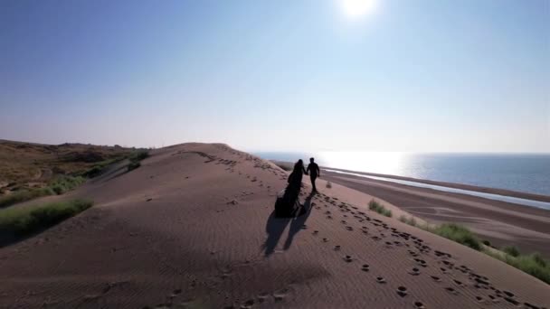 A young couple walk along a sand dune near the sea — Vídeo de Stock