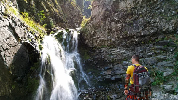 Un ragazzo con uno zaino è in piedi vicino a una cascata — Foto Stock