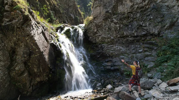 Um cara com uma mochila está parado perto de uma cachoeira — Fotografia de Stock