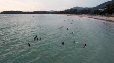 Sörfçüler gün batımında dalga yakalarlar. İnsansız hava aracının görüntüsü