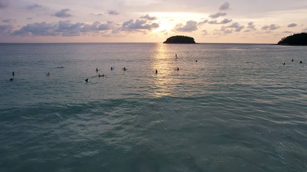 Surfers are waiting for a wave at sunset.