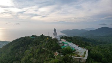 Büyük Buda 'nın insansız hava aracı görüntüsü, Tayland. Büyük Buda, tepede lotus pozisyonunda oturmuş meditasyon yapıyor. Güneş bulutların arasından ışıldıyor. Her yerde bir orman var. Suda bir güneş ışığı