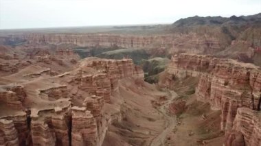 Büyük Kanyon Charyn. Tortul kayalardan kayalar. Kayalarda büyük çatlaklar var. Zemin kırmızı-turuncu. İHA 'nın üst görüntüsü. Merkezde bir yol var. Farklı renklerde yeryüzü katmanları.