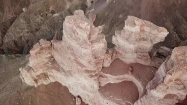 Büyük Kanyon Charyn. Tortul kayalardan kayalar. Kayalarda büyük çatlaklar var. Zemin kırmızı-turuncu. İHA 'nın üst görüntüsü. Merkezde bir yol var. Farklı renklerde yeryüzü katmanları.