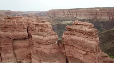 Büyük Kanyon Charyn. Tortul kayalardan kayalar. Kayalarda büyük çatlaklar var. Zemin kırmızı-turuncu. İHA 'nın üst görüntüsü. Merkezde bir yol var. Farklı renklerde yeryüzü katmanları.