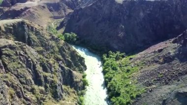 Nehirli Rocky Kanyonu. Ağaçlar kıyıda yetişir. Küçük bir ekolojik ev kampı var. Yüksek uçurumlar, nehir yılan gibi akar. Yukarıdan hava görüntüsü. Charyn Kanyonu. Kazakistan.