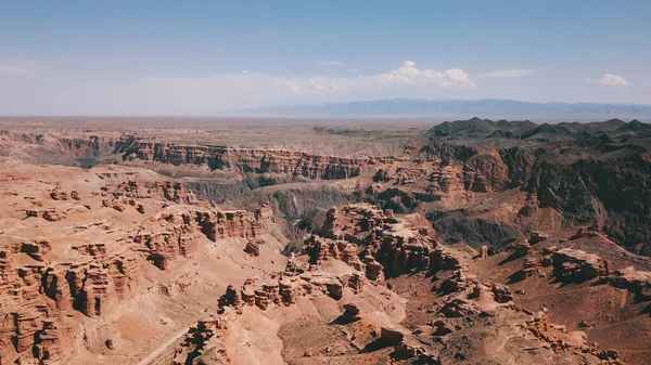 Grand canyon Charyn. Rocks from sedimentary rocks. Huge cracks in the rocks. The ground is red-orange. Top view from a drone. There is a road in the center. Layers of earth in different colors.