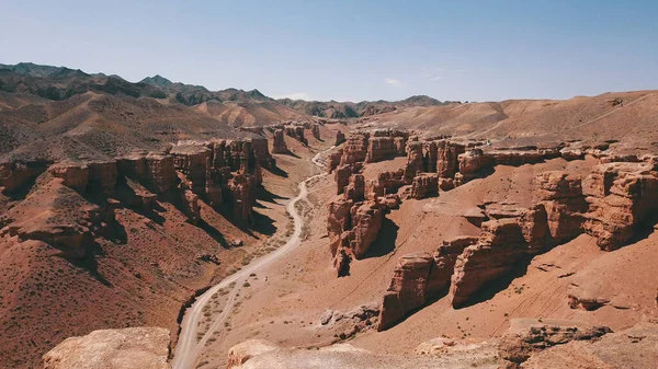 Grand canyon Charyn. Rocks from sedimentary rocks. Huge cracks in the rocks. The ground is red-orange. Top view from a drone. There is a road in the center. Layers of earth in different colors.