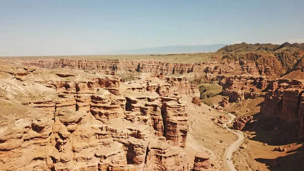 Grand canyon Charyn. Rocks from sedimentary rocks. Huge cracks in the rocks. The ground is red-orange. Top view from a drone. There is a road in the center. Layers of earth in different colors.