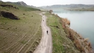 Geniş Nehir ILI. İnsanlar nehir boyunca koşup spor yapıyorlar. İHA 'nın üst görüntüsü. Su yeşil tepeleri, gökyüzünü ve otları yansıtıyordu. Doğada yolda koşmak. Kazakistan.