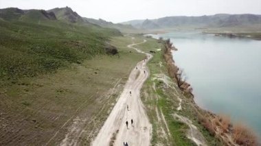 Geniş Nehir ILI. İnsanlar nehir boyunca koşup spor yapıyorlar. İHA 'nın üst görüntüsü. Su yeşil tepeleri, gökyüzünü ve otları yansıtıyordu. Doğada yolda koşmak. Kazakistan.