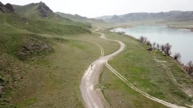 Geniş Nehir ILI. İnsanlar nehir boyunca koşup spor yapıyorlar. İHA 'nın üst görüntüsü. Su yeşil tepeleri, gökyüzünü ve otları yansıtıyordu. Doğada yolda koşmak. Kazakistan.