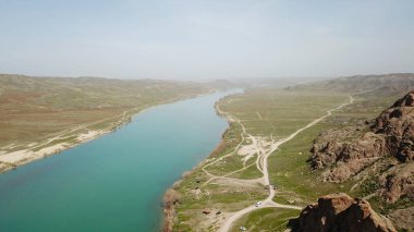 Geniş Nehir ILI. İnsanlar nehir boyunca koşup spor yapıyorlar. İHA 'nın üst görüntüsü. Su yeşil tepeleri, gökyüzünü ve otları yansıtıyordu. Doğada yolda koşmak. Kazakistan.