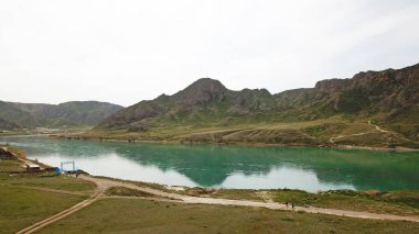 Geniş Nehir ILI. İnsanlar nehir boyunca koşup spor yapıyorlar. İHA 'nın üst görüntüsü. Su yeşil tepeleri, gökyüzünü ve otları yansıtıyordu. Doğada yolda koşmak. Kazakistan.