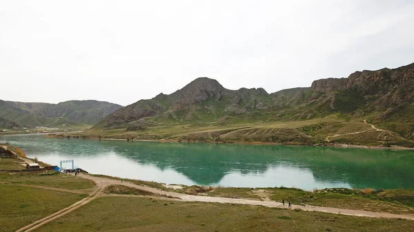 Geniş Nehir ILI. İnsanlar nehir boyunca koşup spor yapıyorlar. İHA 'nın üst görüntüsü. Su yeşil tepeleri, gökyüzünü ve otları yansıtıyordu. Doğada yolda koşmak. Kazakistan.