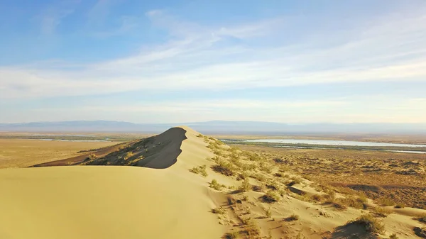 Huge sand dunes of Kazakhstan. Top view from a drone on a singing dune. A group of people are resting on the top of a mountain. A lot of yellow sand, traces of people are visible. Blue sky with clouds