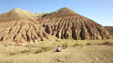 Renkli dağların arasında meditasyon. Çölün ortasındaki kireçtaşı dağları. Beyazdan kırmızıya renkli tepeler. Adam oturur ve Altyn Emel kanyonunun doğasını düşünür. Kazakistan.